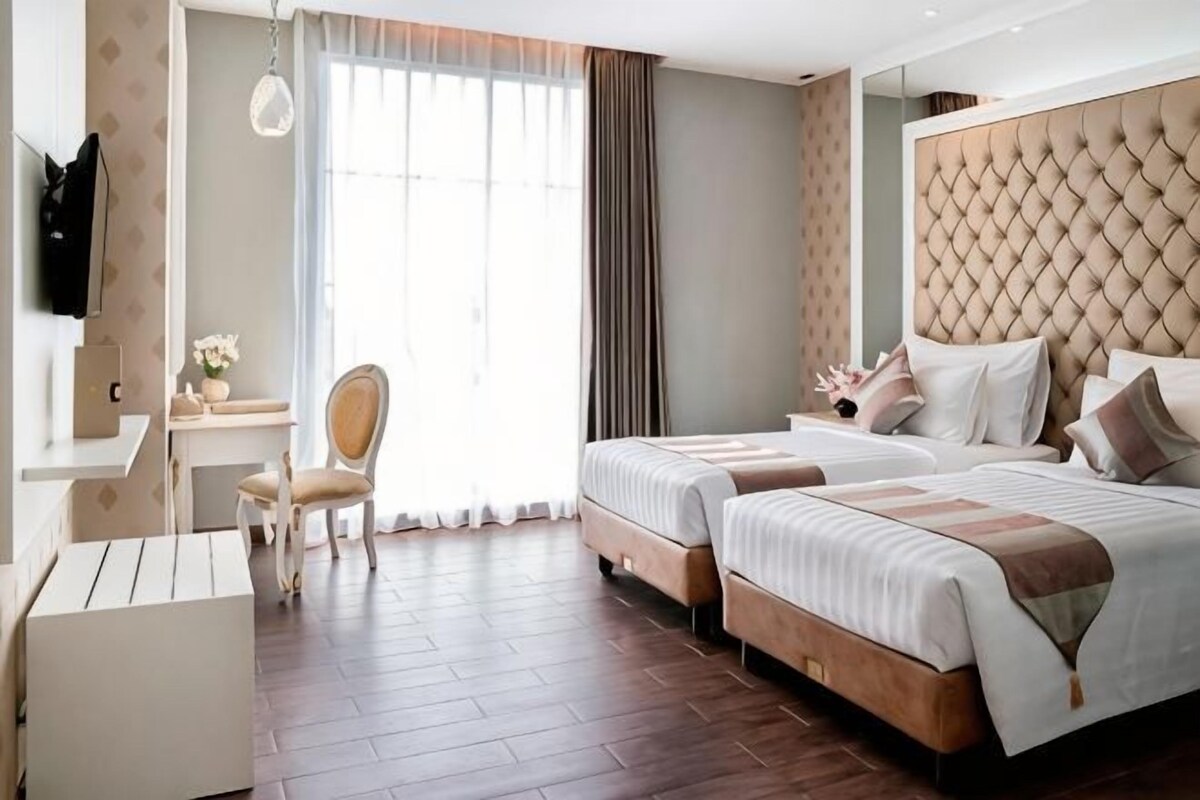 A hotel room with two beds, a desk, a chair, and a television.