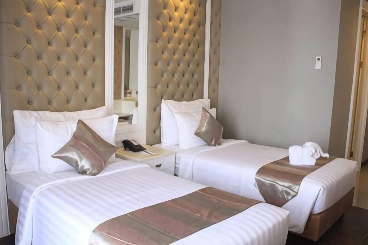 Habitación de hotel con dos camas, cabecera capitonada, mesita de noche con lámpara y espejo.
