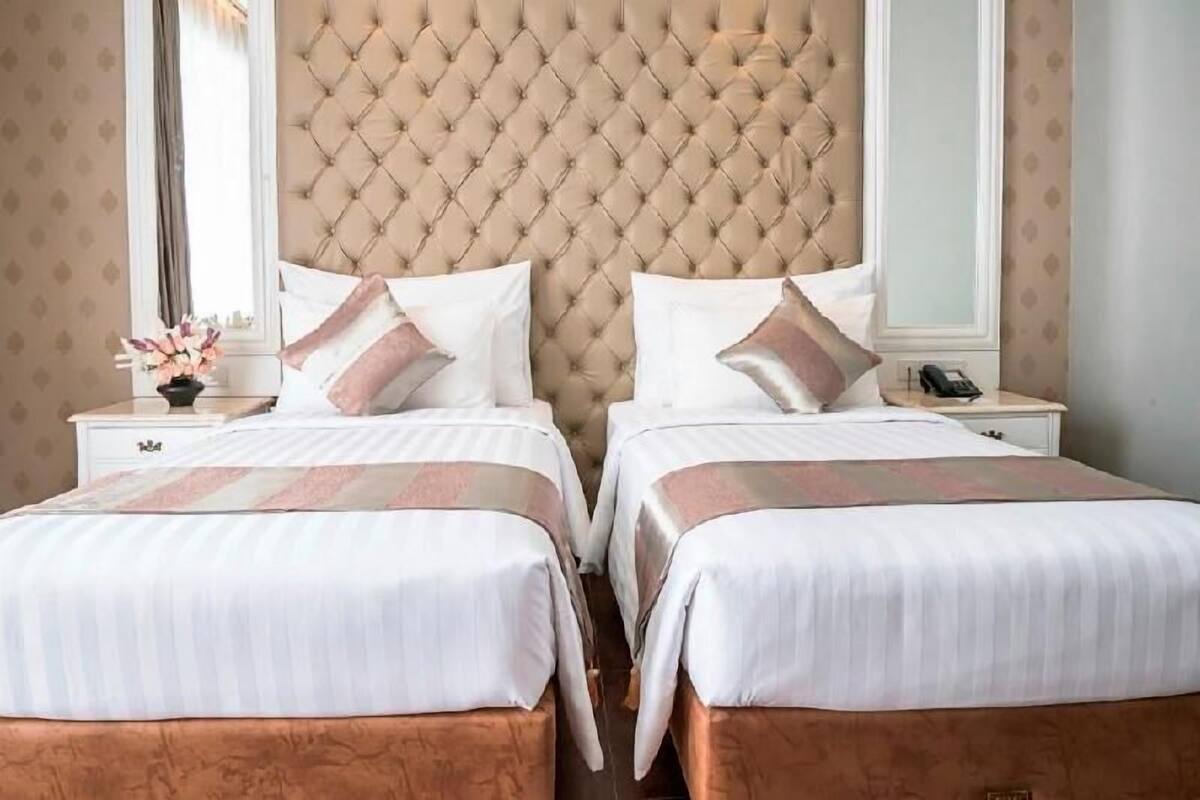 Una cama doble con cabecera capitonada, dos mesitas de noche con lámparas y un espejo.