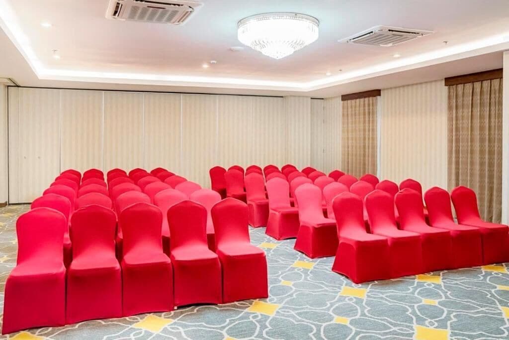 Une salle de conférence avec des rangées de chaises rouges et un tapis à motifs.