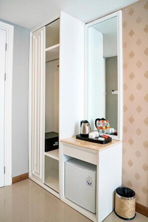 Ein Zimmer mit einem weißen Kleiderschrank, einem Spiegel, einem kleinen Tisch mit Wasserkocher, Tassen und Flaschen sowie einem Mülleimer.