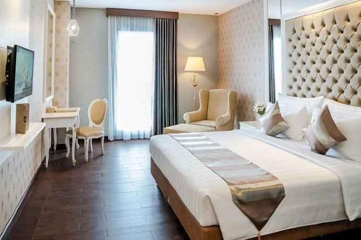 A hotel room with a large bed, two armchairs, a desk, and a television.