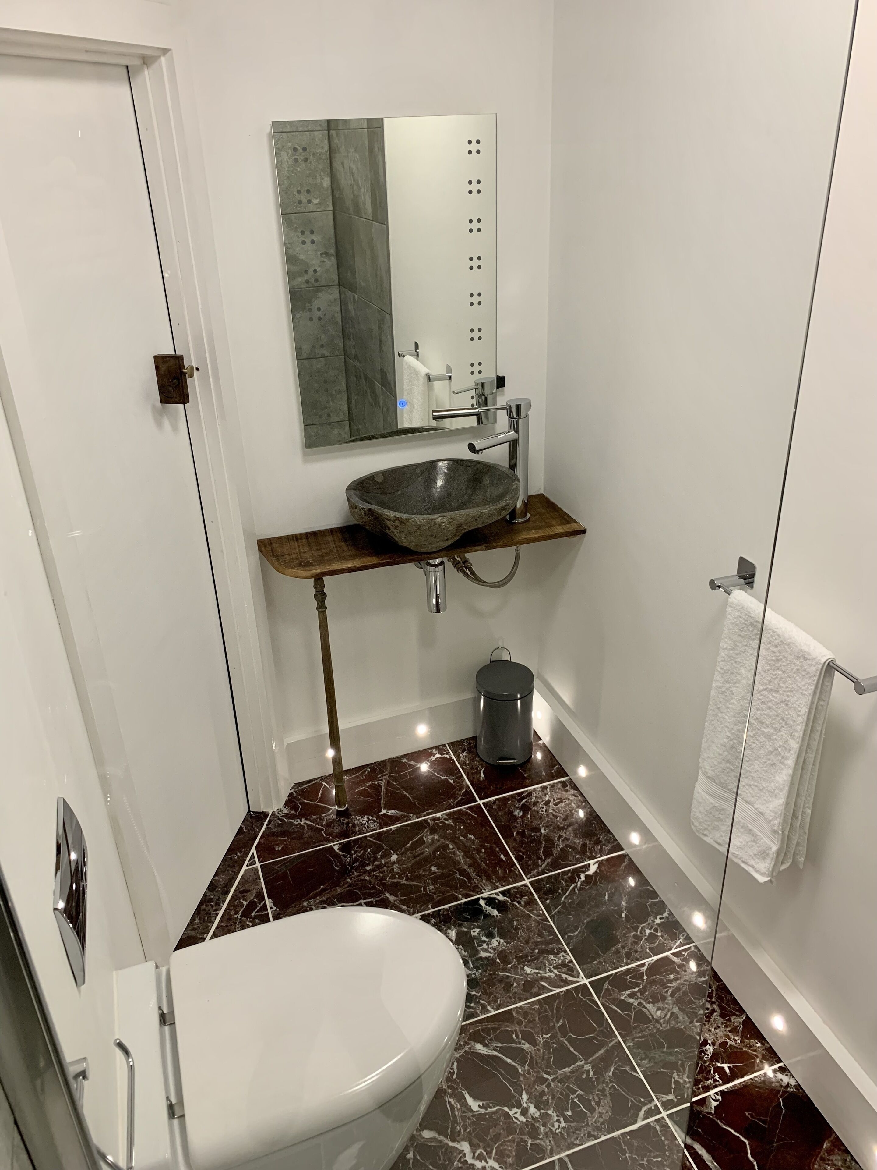 Un bagno con il water bianco, un lavabo a incasso su un piano in legno, uno specchio e un porta asciugamani.