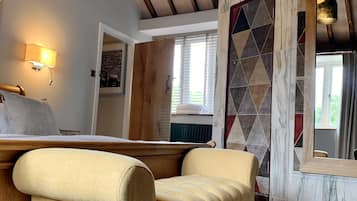 A cozy room with a wooden ceiling, a bed with a headboard, a beige armchair, and a patterned wall.