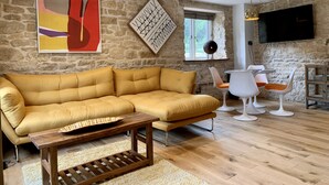 A modern living room with a stone wall, a large abstract painting, a wooden coffee table, and a seating area with white chairs and a yellow sofa. - The Coach House and The Stable (Stroud)