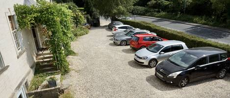 A gravel parking area with several cars parked in front of a building with steps leading up to the entrance.