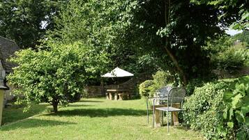 A garden with a picnic table and chairs, surrounded by trees and a stone wall.