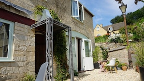 A stone building with a covered patio, outdoor seating, and a garden area. - The Coach House and The Stable (Stroud)