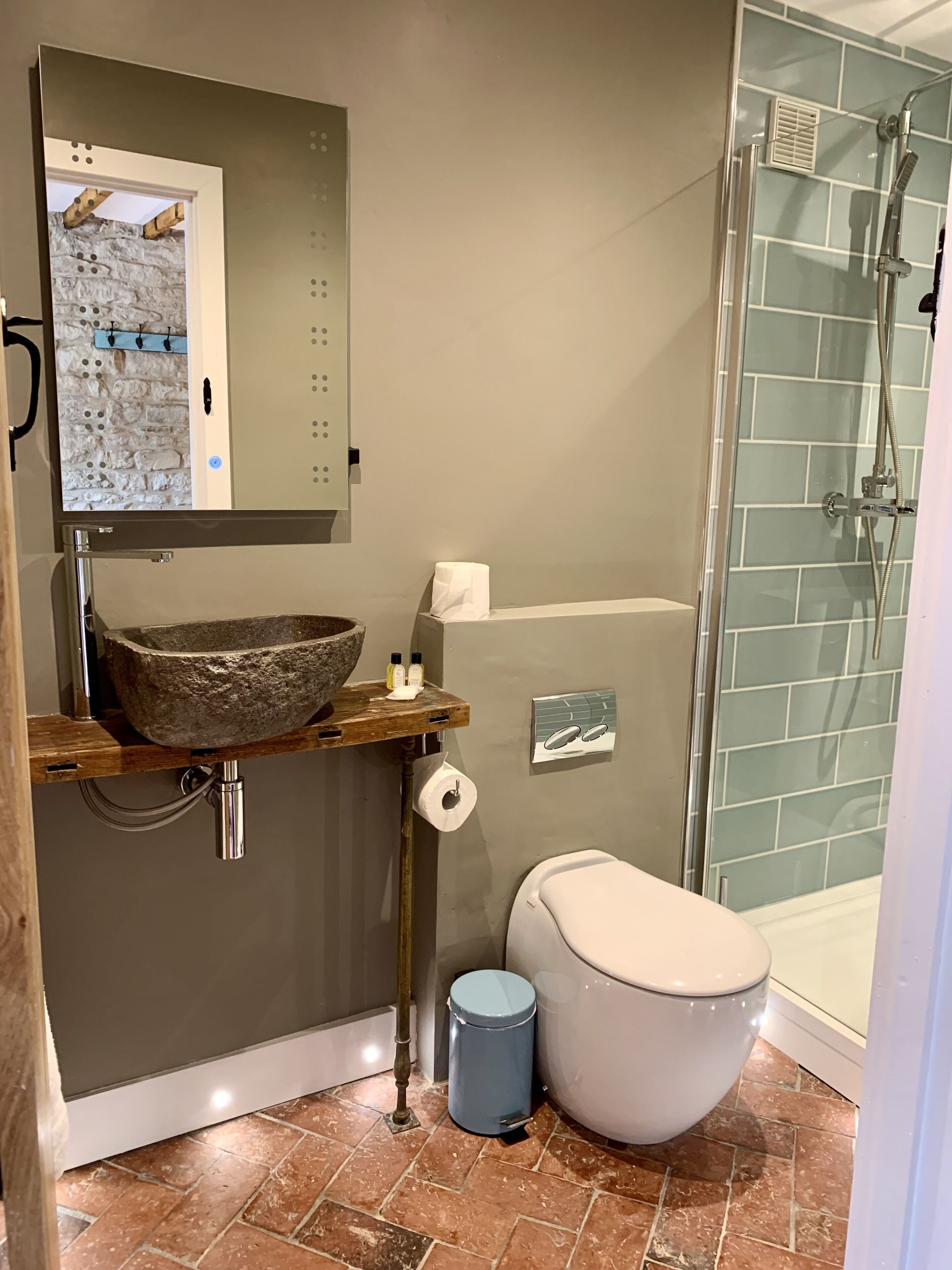 Een badkamer met een wastafel van steen, een toilet en een douchecabine met glazen wanden.