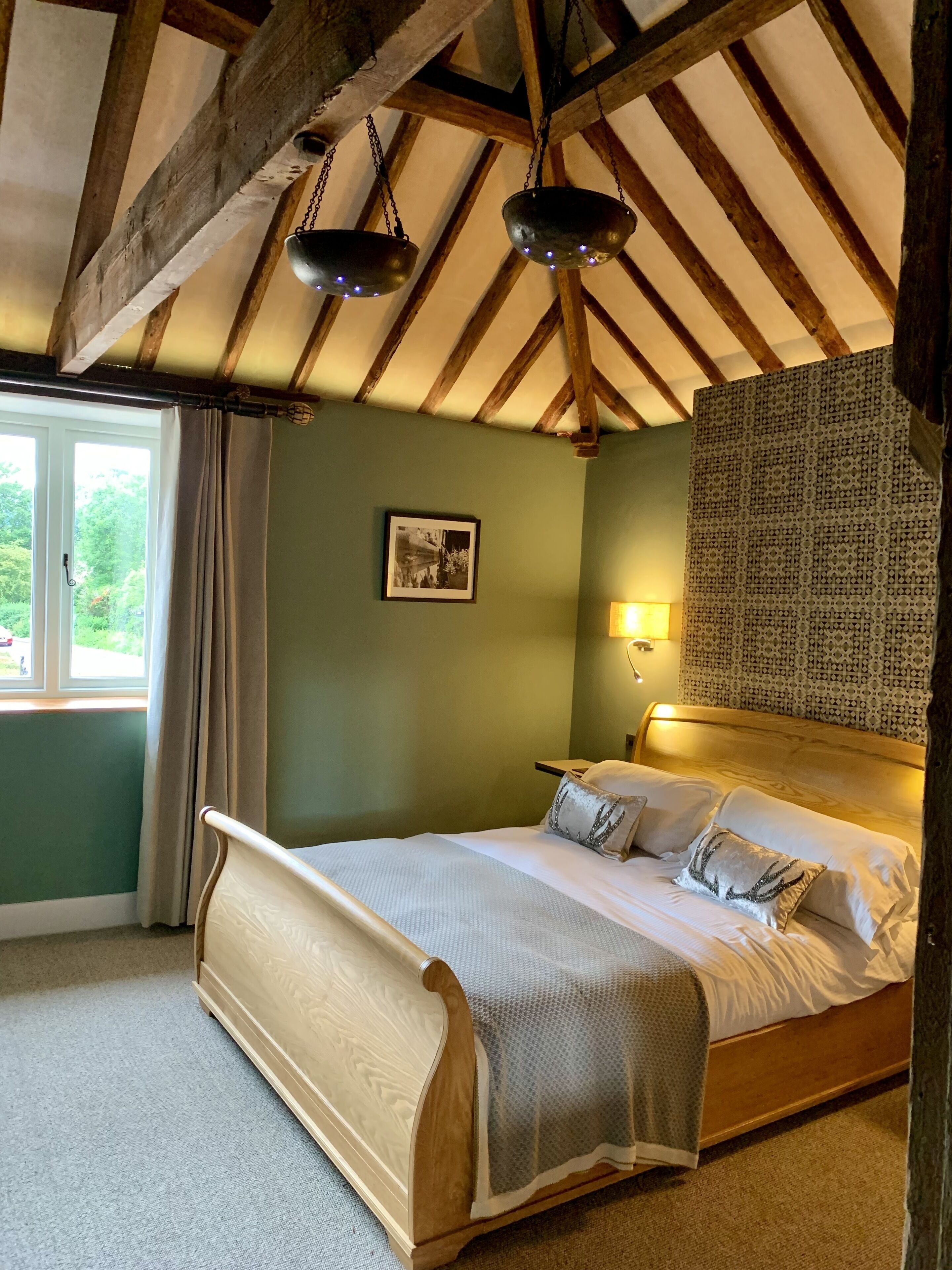 A bedroom with a wooden bed, a window with curtains, a wall-mounted lamp, and a patterned wall.