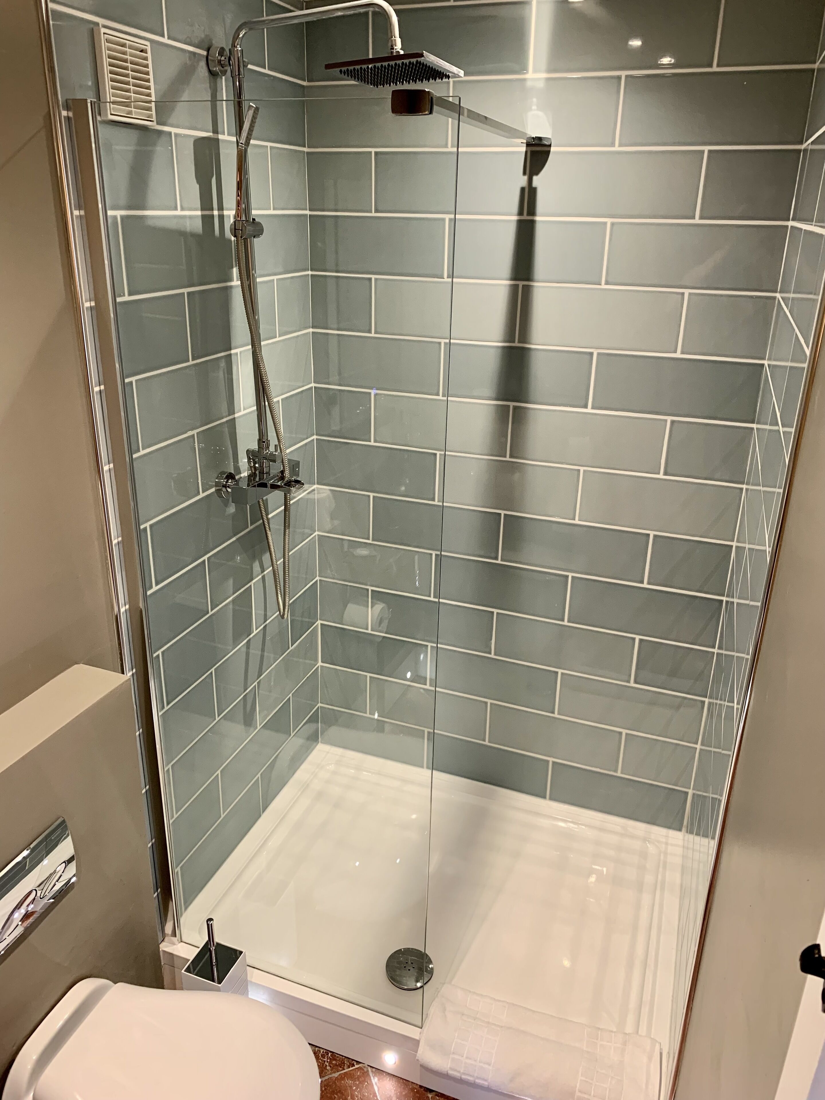 A glass-enclosed shower with a handheld showerhead and a fixed showerhead.