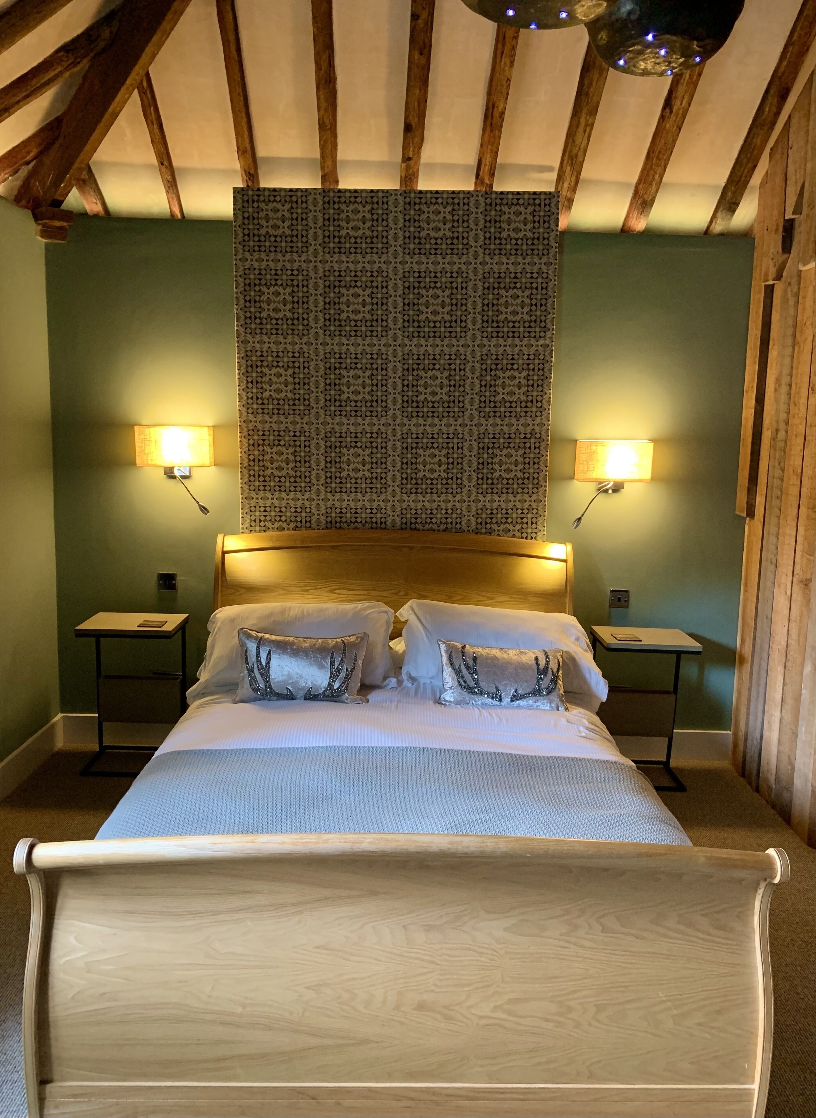 A bedroom with a wooden bed, two bedside tables, patterned wall hanging, and wall-mounted lamps.