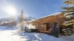 A wooden cabin with a sauna, surrounded by snow-covered trees and mountains.