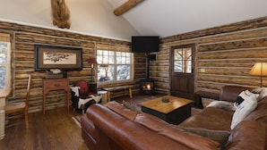 A log cabin interior with a fireplace, leather sofa, and a mounted deer head.