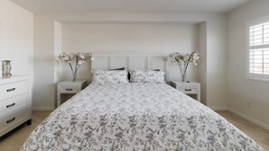A bedroom with a large bed, two nightstands, a dresser, and a window.