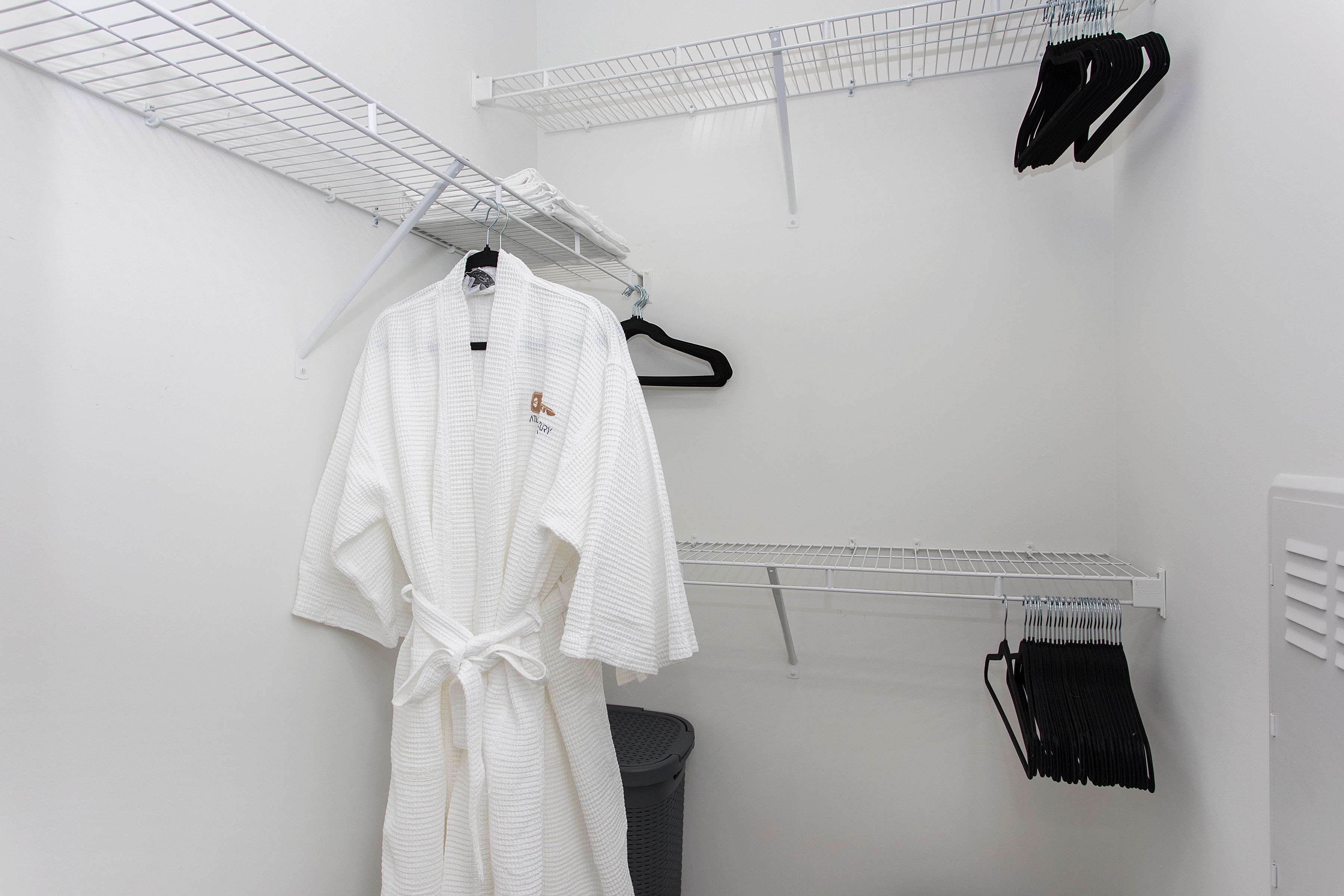 A white robe hanging on a rack in a room with white walls and a grey trash bin.