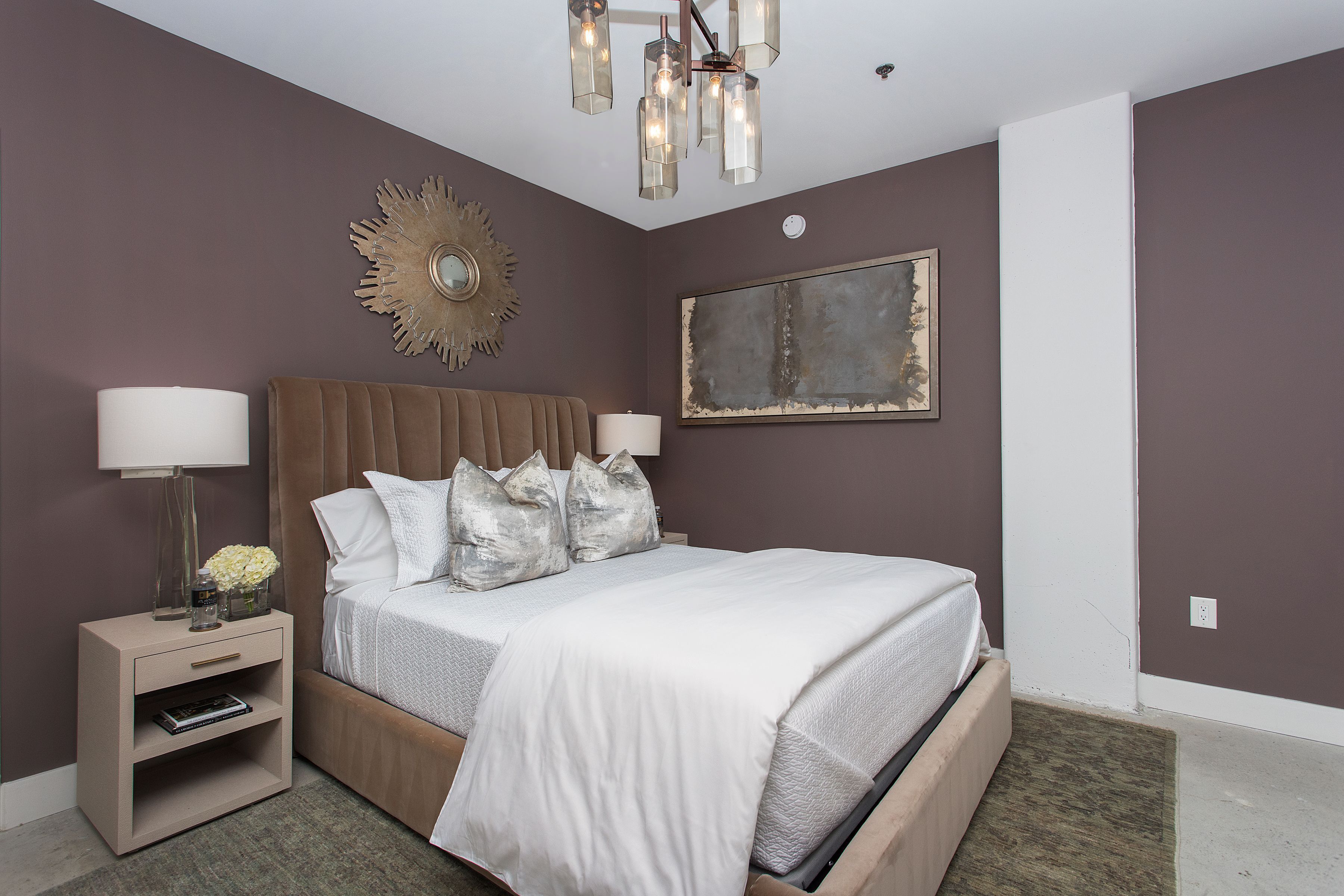 A bedroom with a large bed, bedside tables, a chandelier, and a wall-mounted mirror.