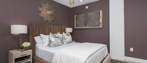 A bedroom with a large bed, bedside tables, a chandelier, and a wall-mounted mirror.