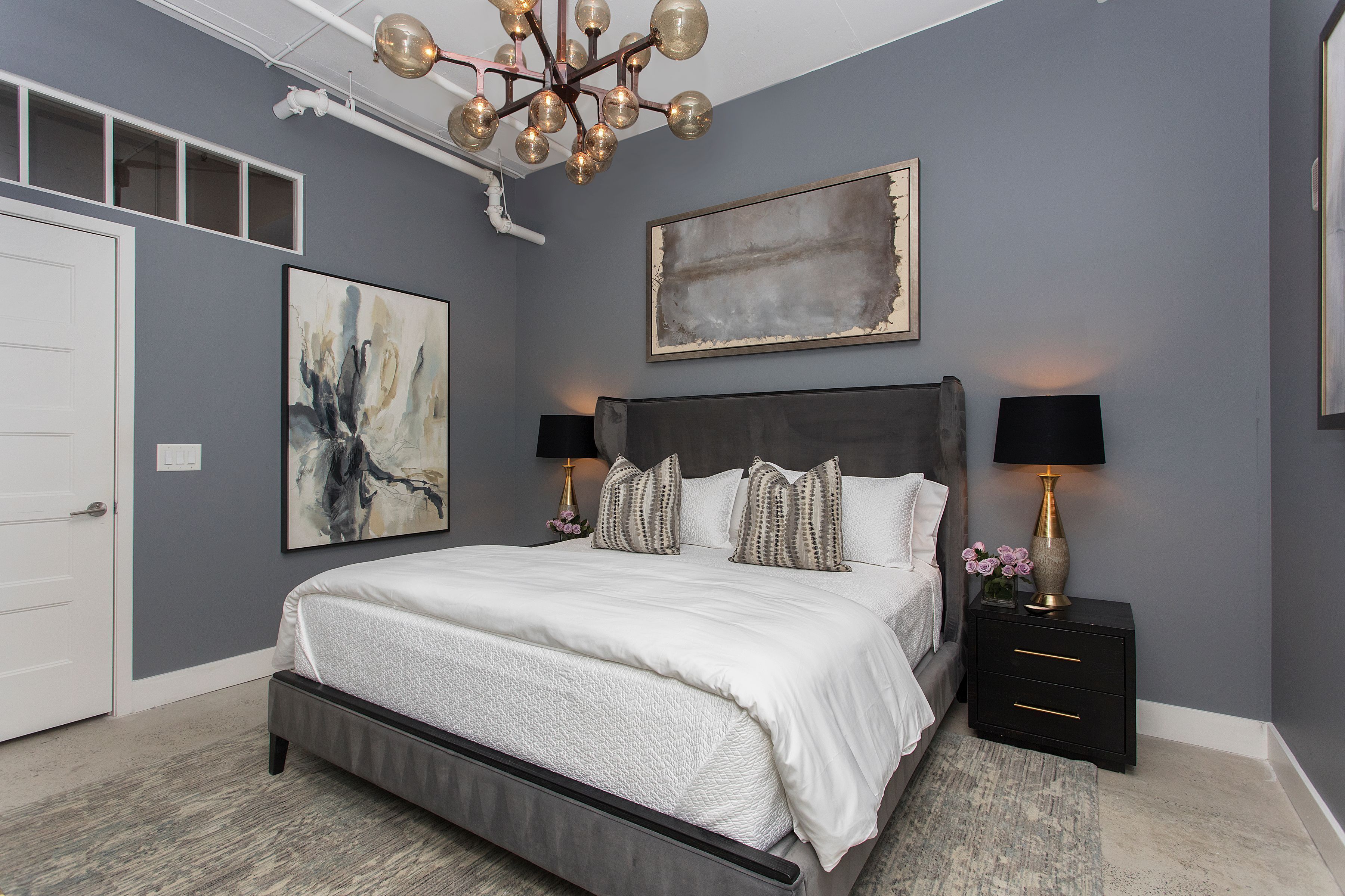 A modern bedroom with a large bed, two bedside tables, a chandelier, and artwork on the walls.