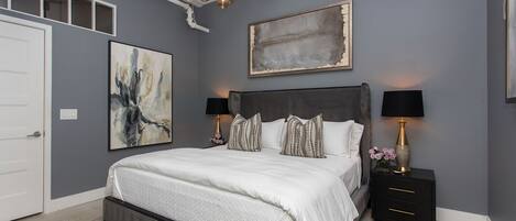 A modern bedroom with a large bed, two bedside tables, a chandelier, and artwork on the walls.