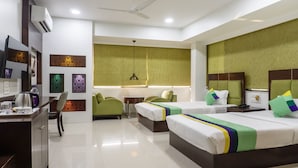 A hotel room with two beds, a desk with a kettle, a chair, a small table, and decorative panels on the wall. - Treebo Bhairavee, Baner (Pune)