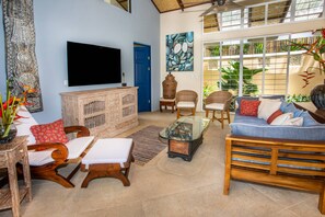 A spacious living room with a television, wicker furniture, and a large window with plants.