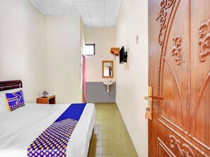 A hotel room with a bed, a bedside table, a wooden door, a bathroom with a sink, and a mirror.