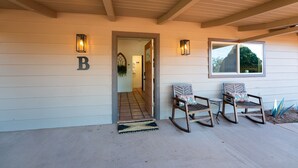 A house entrance with a wooden porch, two rocking chairs, a door marked with a 'B', and two wall-mounted lights. - Remodeled, Centrally Located in Sedona 2 Bed / 2 Bath Home (Sedona)