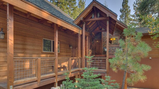 Une cabane en bois dotée d’un porche couvert, d’une cheminée en pierre et d’un petit jardin où se trouve un pin.