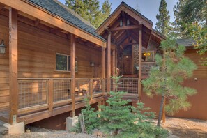 A wooden cabin with a covered porch, a stone fireplace, and a small garden with a pine tree. - Tahoe Rim Retreat - Large 3BR + Bonus Rooms with Pool Table and Private Hot Tub - Pet Friendly! (Kings Beach)