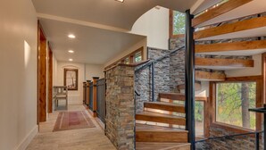 Un escalier moderne avec des marches en bois et des éléments décoratifs en pierre, menant à un deuxième étage doté de grandes fenêtres et offrant une vue sur les arbres.