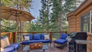 Une terrasse en bois avec un ensemble de meubles de jardin bleu, un barbecue et une table décorée de pommes de pin.