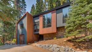 A modern two-story house with a stone foundation, large windows, and a wooden facade. - Mod Haus by Tahoe Getaways - West Shore w/ Private Beach Access & Pier + Close to Lake! (Homewood)
