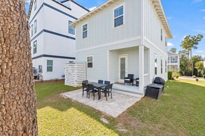 A two-story house with a patio area featuring a table and chairs, a grill, and a covered seating area.
