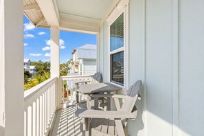 Un balcon avec une table et des chaises, une fenêtre avec des stores et une vue sur les maisons voisines.