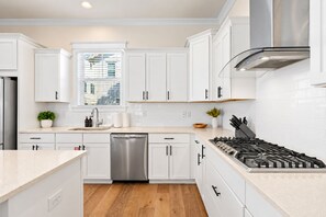 A modern kitchen with white cabinetry, a stainless steel dishwasher, a gas stove, and a window with blinds. - Casa Del Sol - 3BR/2.5BA Grande Pointe Home - Sleeps 9 - Community Pool (Inlet Beach)