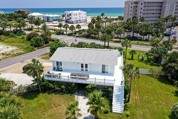 Una casa blanca de dos pisos con balcón, rodeada de palmeras y vista a la playa.