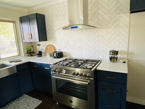 Una cocina moderna con estufa de acero inoxidable, armarios azul oscuro y salpicadero blanco con patrón de espiga.
