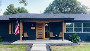 Une maison à l’extérieur bleu foncé, avec une porte d’entrée en bois et le numéro « 3510 » au-dessus. On y voit deux chaises à l’extérieur, un drapeau américain et une petite table avec une plante.