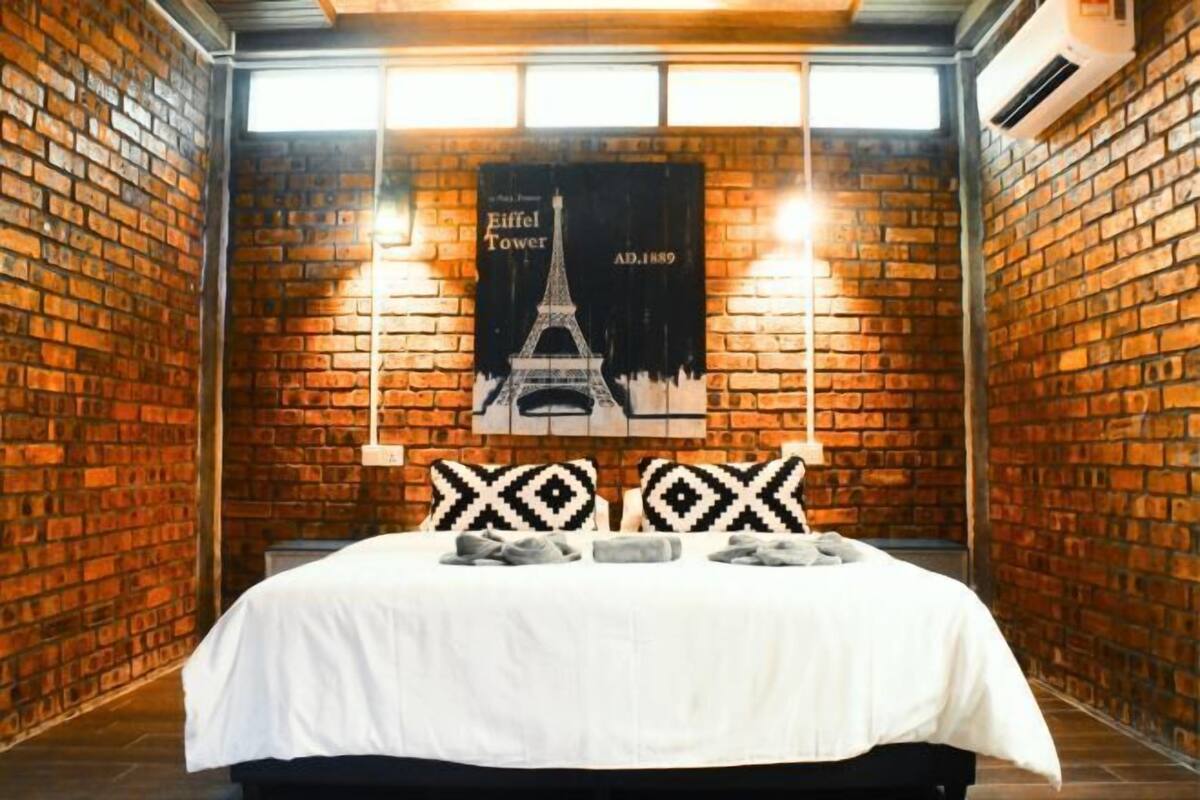 Habitació amb paret de maó, llit amb roba de llit blanca, dos almoinades estampades i un cartell de la Torre Eiffel.