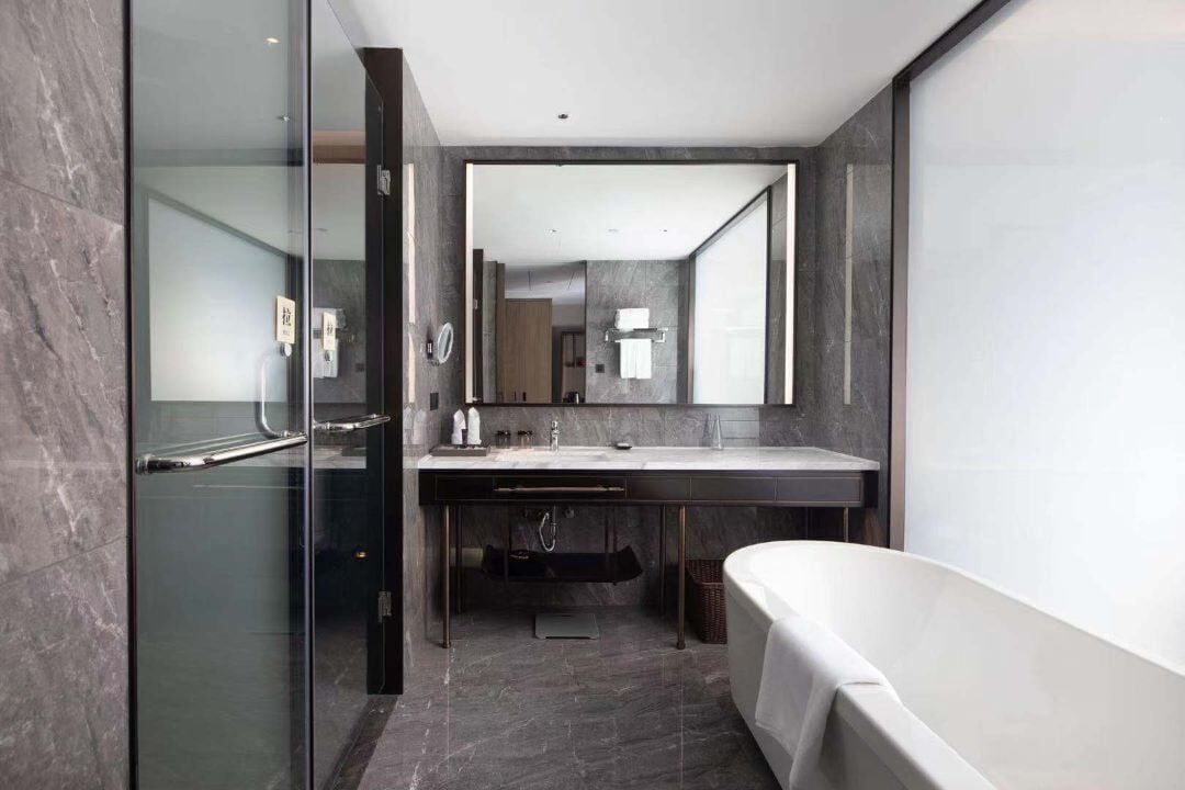A modern bathroom with a glass shower enclosure, a freestanding bathtub, and a large mirror above the sink.