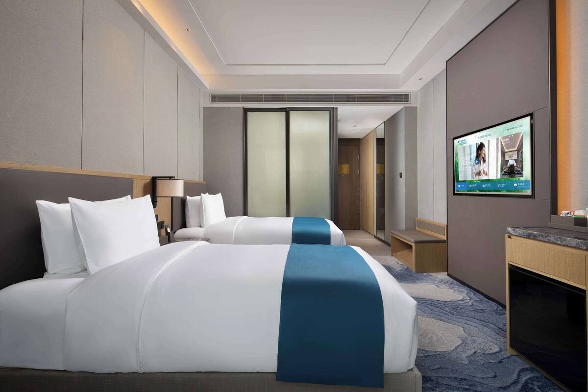 Una habitación de hotel con una cama grande, un televisor montado en la pared y un escritorio con una computadora.