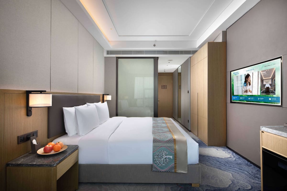 Una habitación de hotel con una cama, una mesita de noche con fruta, un televisor y un espejo.
