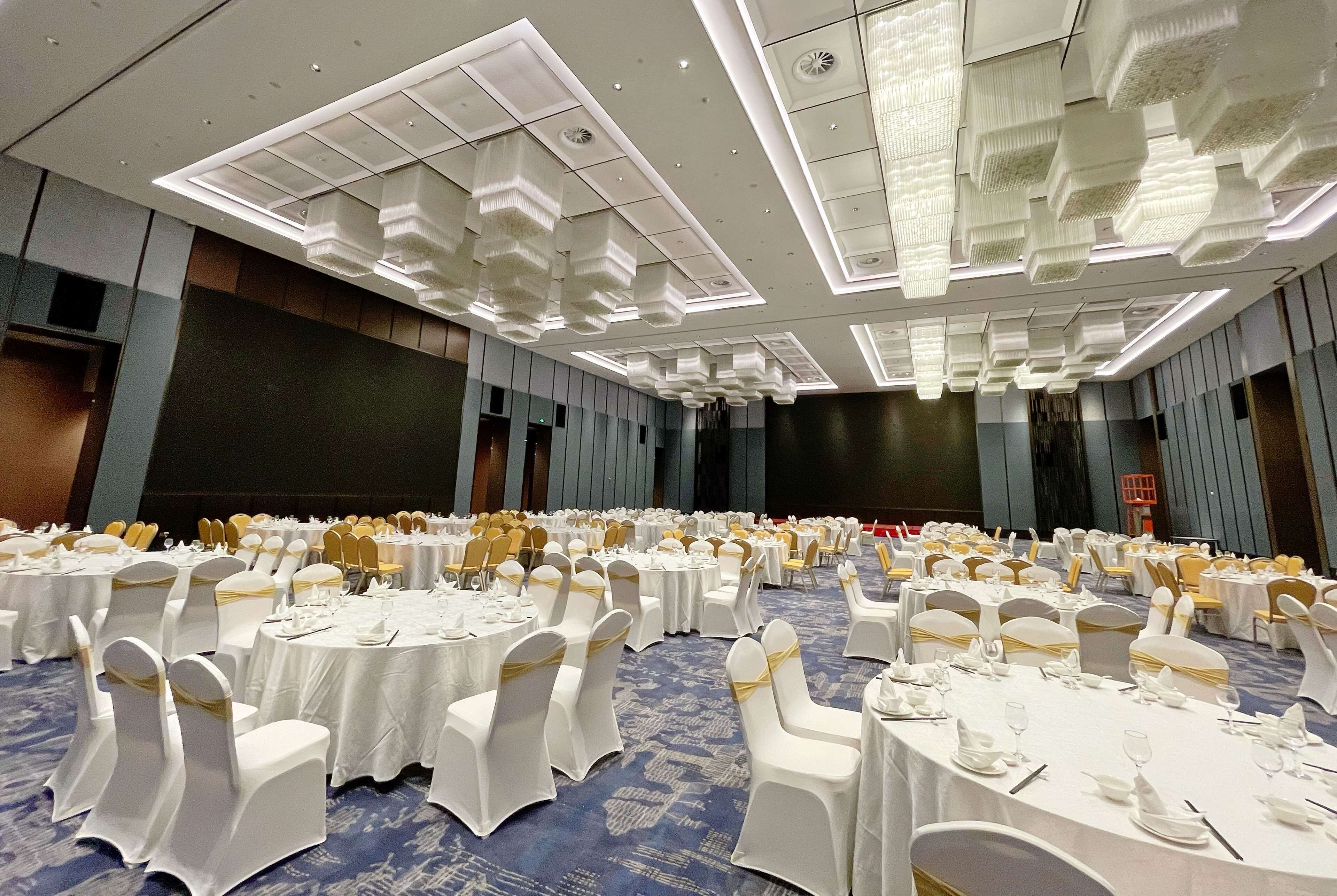 A banquet hall with round tables, white tablecloths, and chairs with gold sashes.