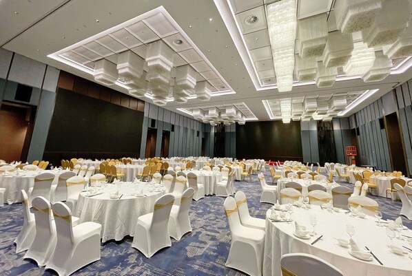 Un salón de banquetes con mesas redondas, manteles blancos y sillas con cintas doradas.