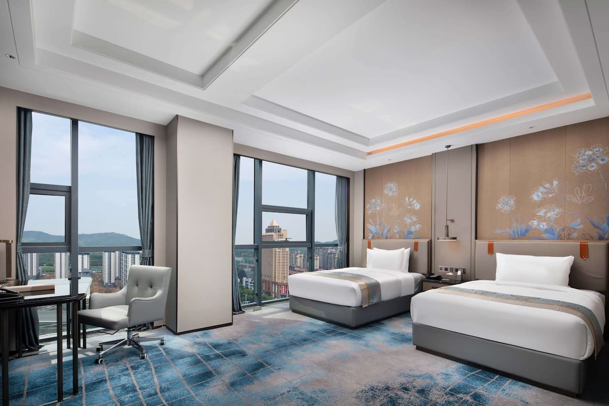 Habitación de hotel con dos camas, un escritorio y una silla. Amplias ventanas con vistas a la ciudad.