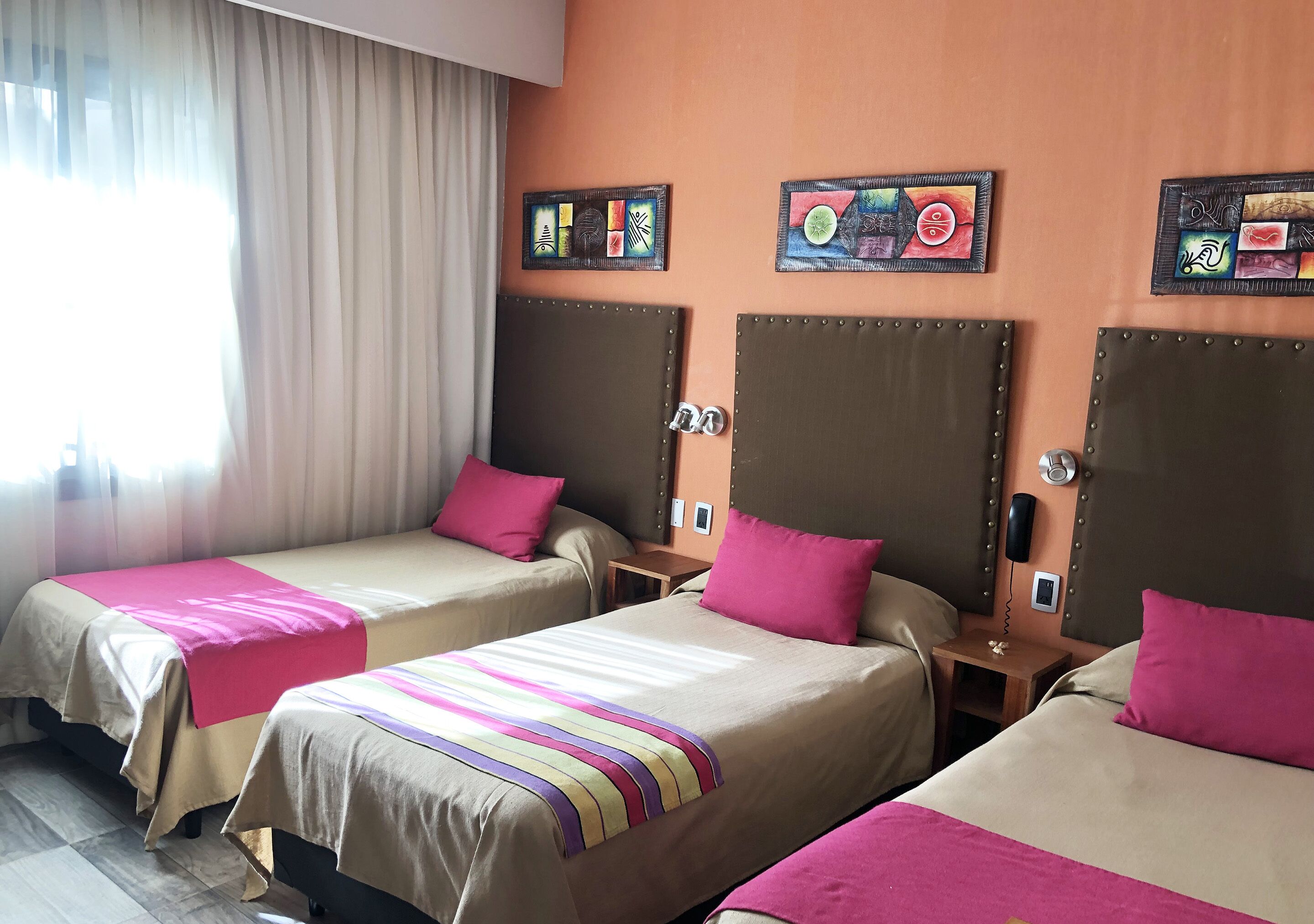A hotel room with two beds, each with a headboard and a bedside table. There are decorative wall art pieces above the beds.
