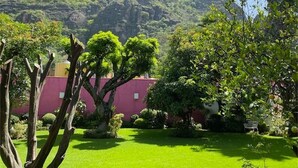 A lush garden with a variety of trees and shrubs, a red building, and a mountainous backdrop. - Finca El Paraiso  (Tepoztlán)