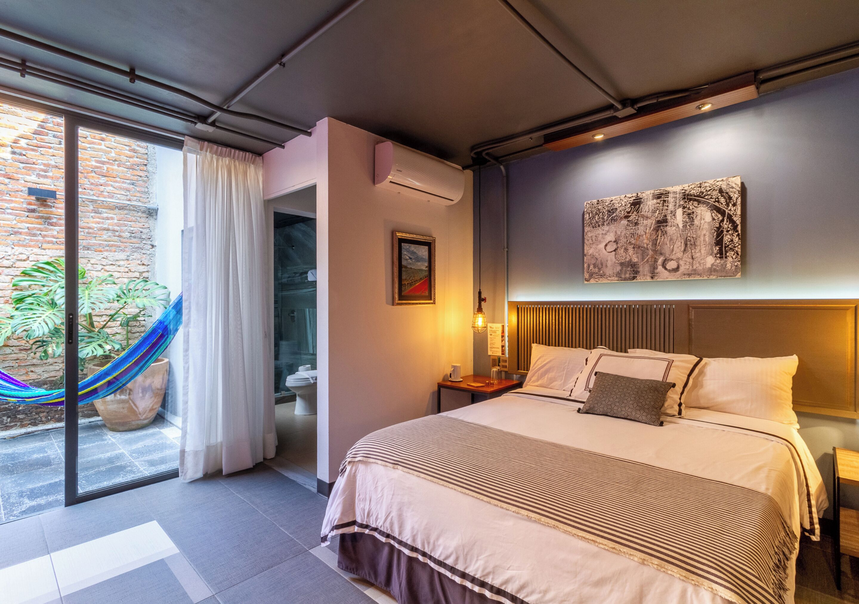 Une chambre d’hôtel moderne avec un grand lit, une vue sur l’extérieur, un hamac et un tableau au mur.