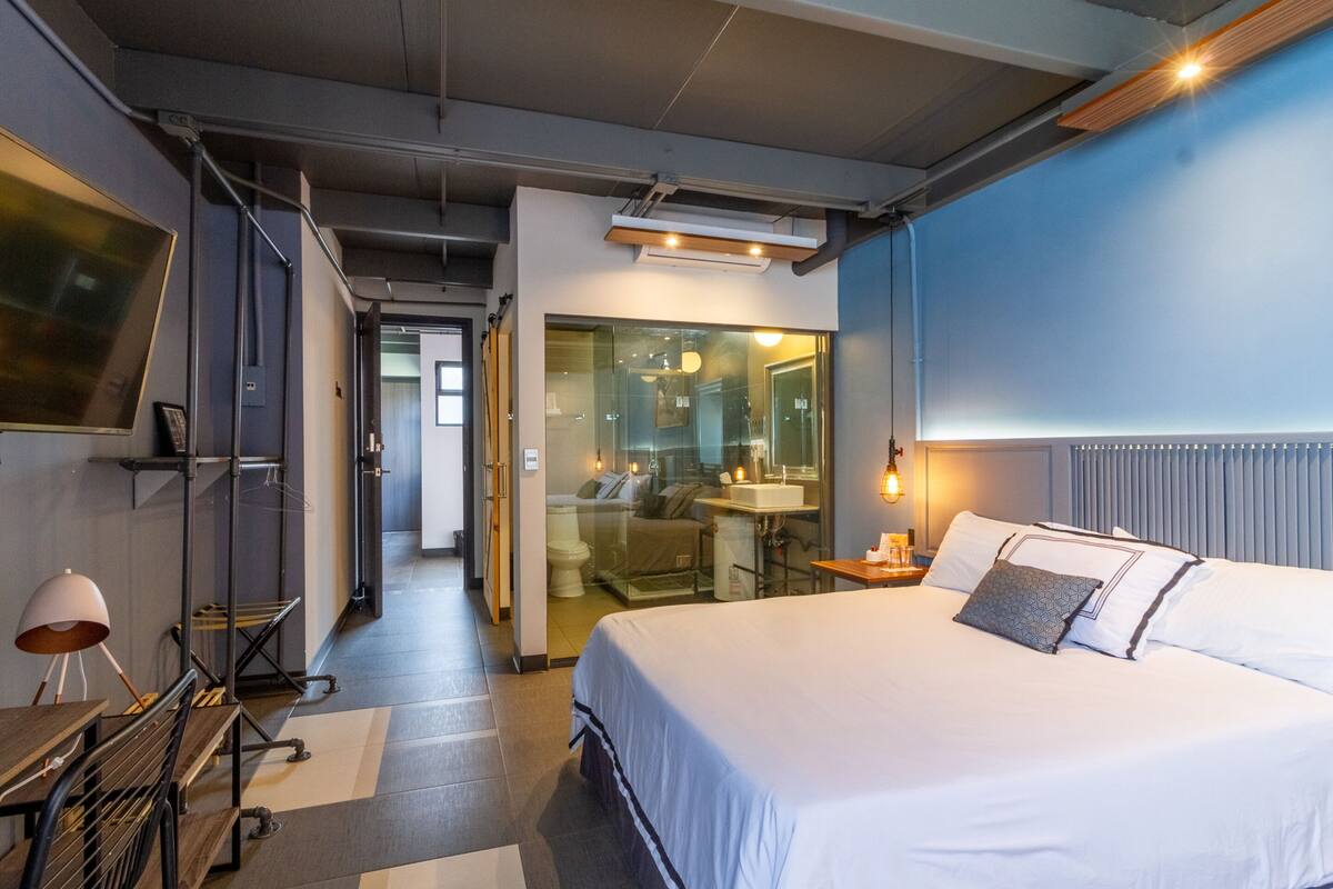 Une chambre d’hôtel moderne avec un grand lit, un bureau, une chaise, une lampe de bureau et un grand miroir.